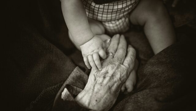 Babyhand und Hand einer älteren Person, Hände altern schneller als das Gesicht